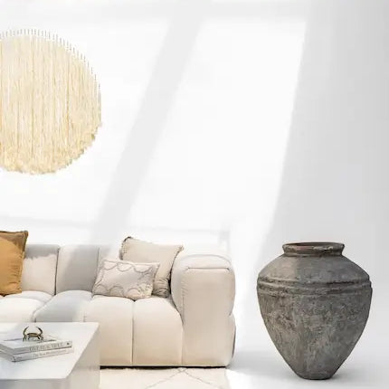 Beige modular sofa with a large aged stone floor vase in a bright room