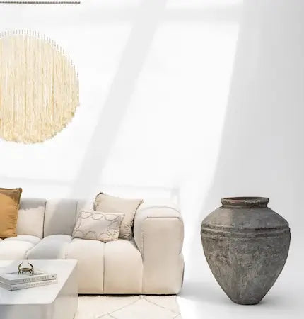 Beige modular sofa with a large aged stone floor vase in a bright room