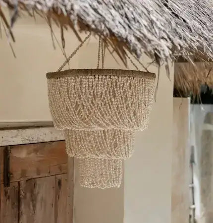 Handwoven beaded chandelier hanging under thatched roof, natural coastal lighting in Bali-inspired outdoor space