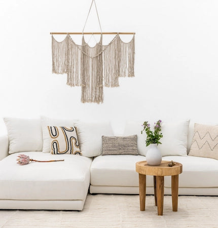 Macrame wall hanging above a white sofa with a wooden side table