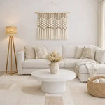 Minimalist beige living room with white sofa, round coffee table and macrame wall decor