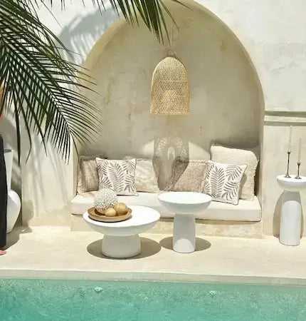 Rattan pendant light above arched seating nook with concrete side tables, neutral boho outdoor styling by the pool