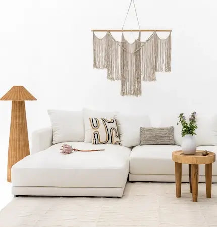 White L-shape sofa styled with rattan floor lamp and boho macrame wall decoration