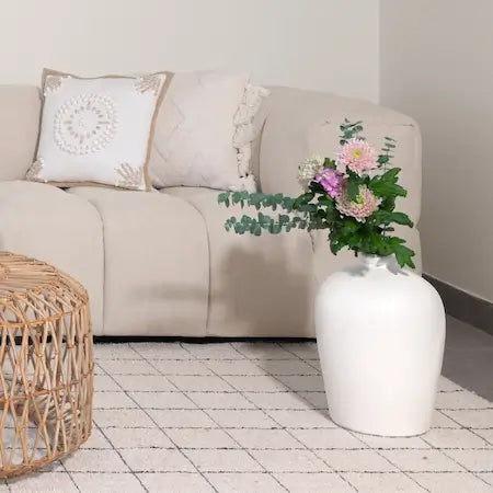 White ceramic floor vase with flowers beside a beige sofa and rattan table