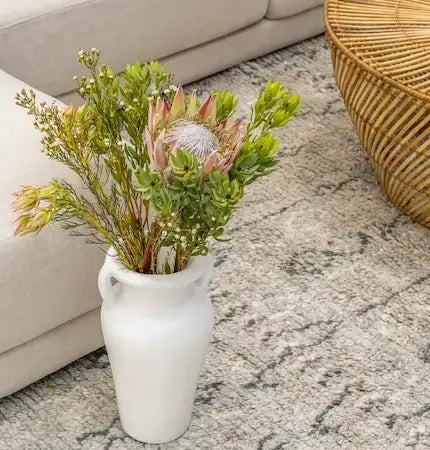 White ceramic handled vase with a protea and greenery bouquet on a textured rug- summer sale Dubai